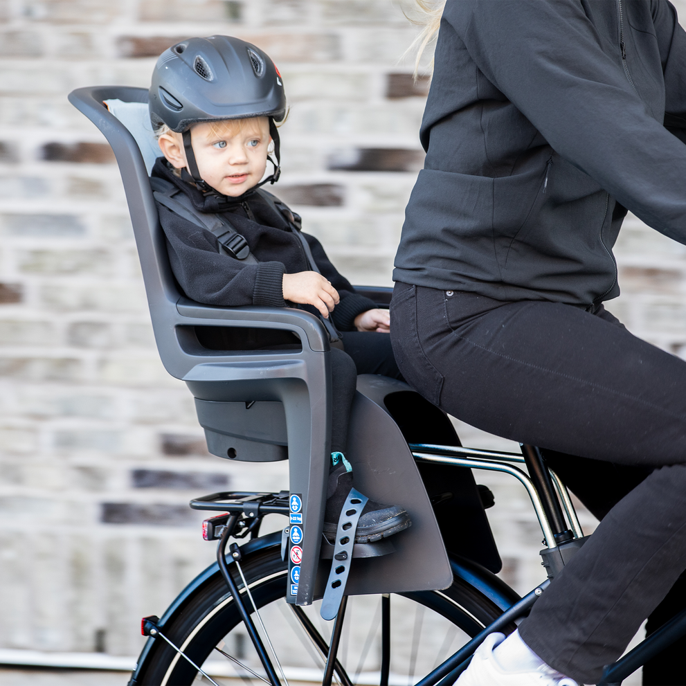 A child sits in a Thule RideAlong2 child bike seat as their parents cycles.