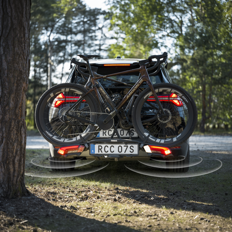 Rear view of a car with a Thule Epos ParkSecure bike carrier mounted on the towbar, carrying a road bike with the parking sensors on.