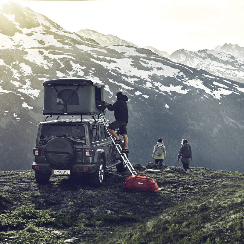 A man is climbing into a roof top tent mounted on a car in the mountains