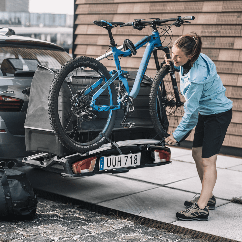 A woman loads a bike next to her trunk cargo box using the Thule VeloSpace XT Bike Adapter.