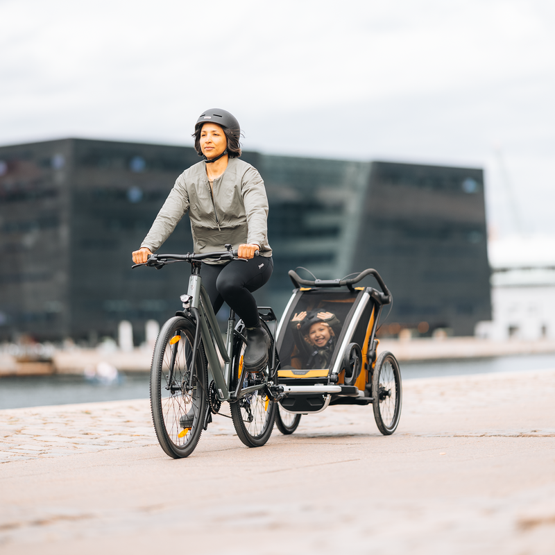 Person cycling through the city with a Thule Chariot Sport 2 bike trailer, combining active transport with everyday convenience.