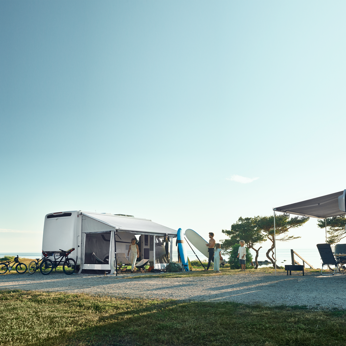 Two motorhomes parked in the countryside have a Thule Residence G3 rv awning tent.
