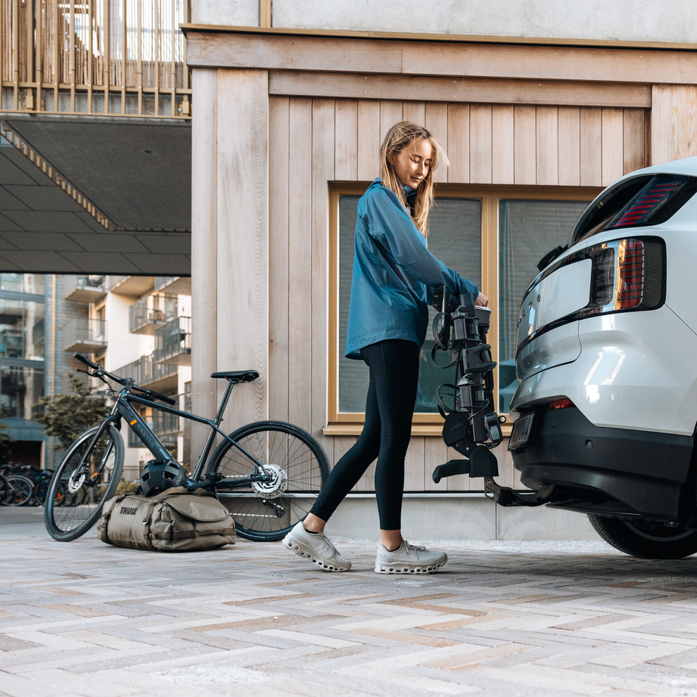A woman is placing a Thule Outpace towbar bike carrier on the towbar on a white car.