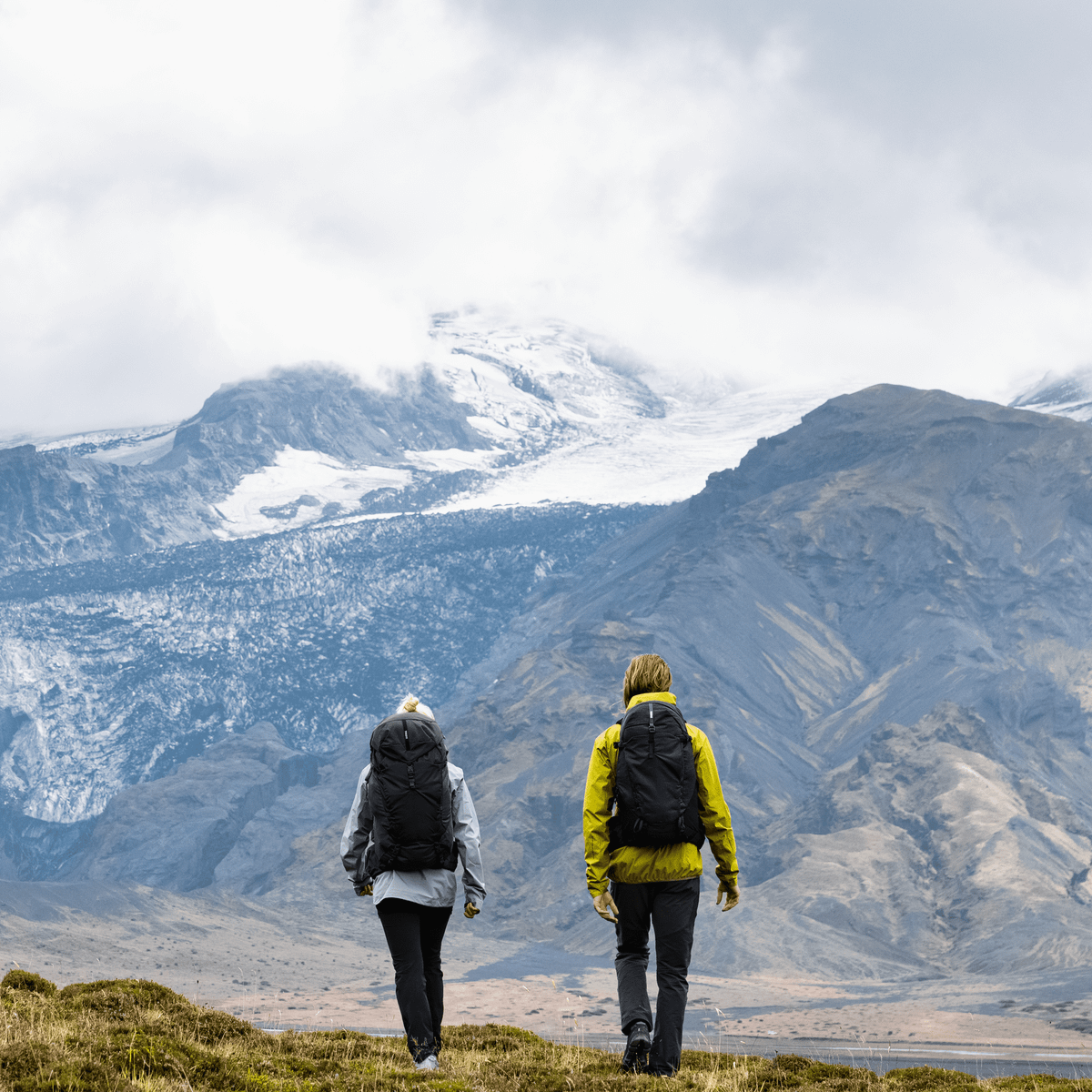 A man and woman walk towards a mountain carrying Thule Topio 30L hiking backpacks.