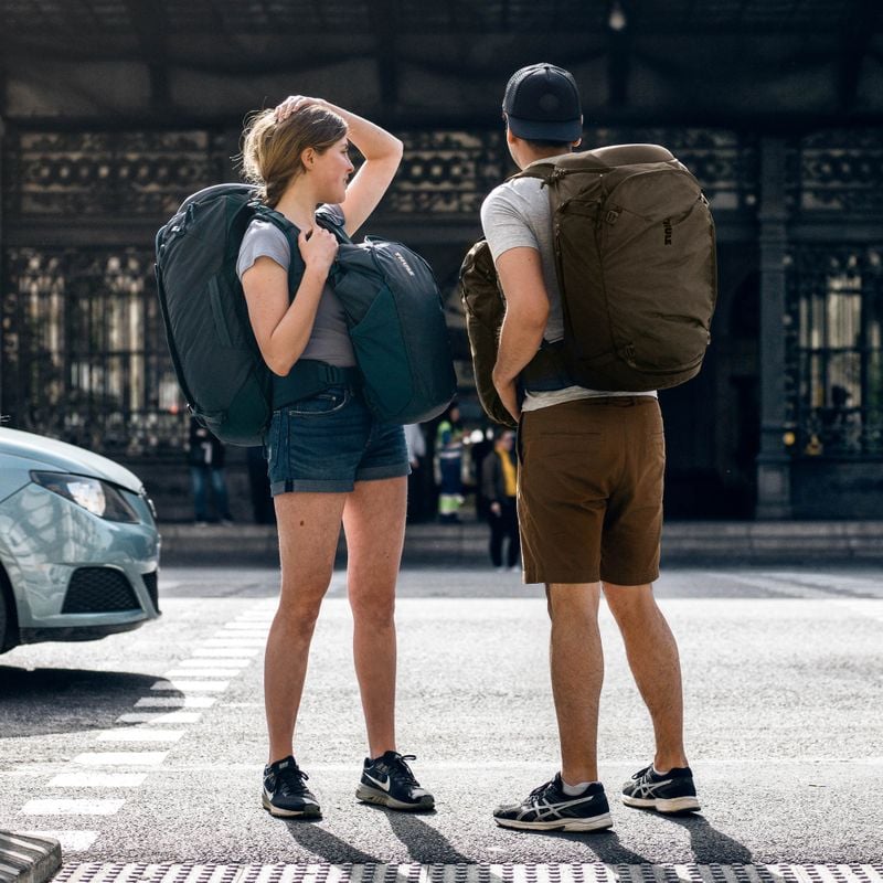 A couple stand on the street outside a train station carrying Thule Landmark 60L travel backpacks.