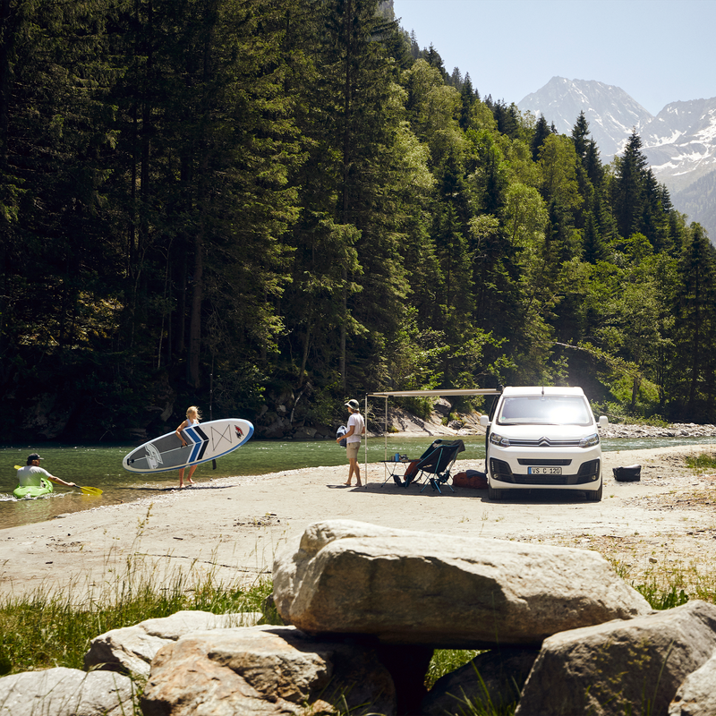 A van parked in the mountains next to the river with a Thule 3200 van awning.