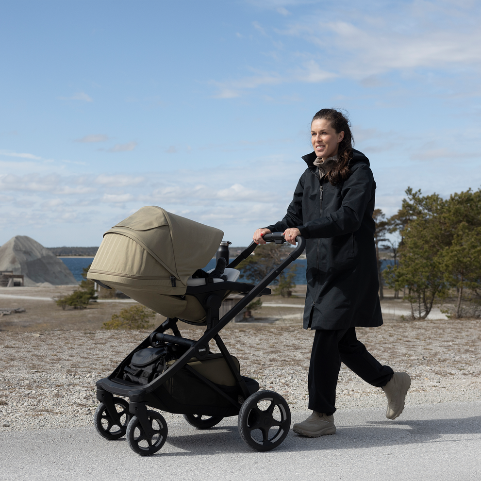 Adult pushing a Thule Charm stroller outdoors by the water.