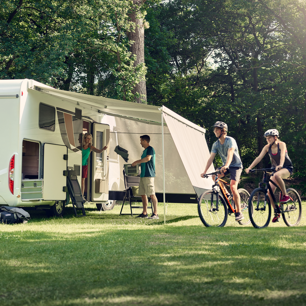 White rvs parked in the grass where families are walking around with a Thule Sun Blocker Side awning side wall.