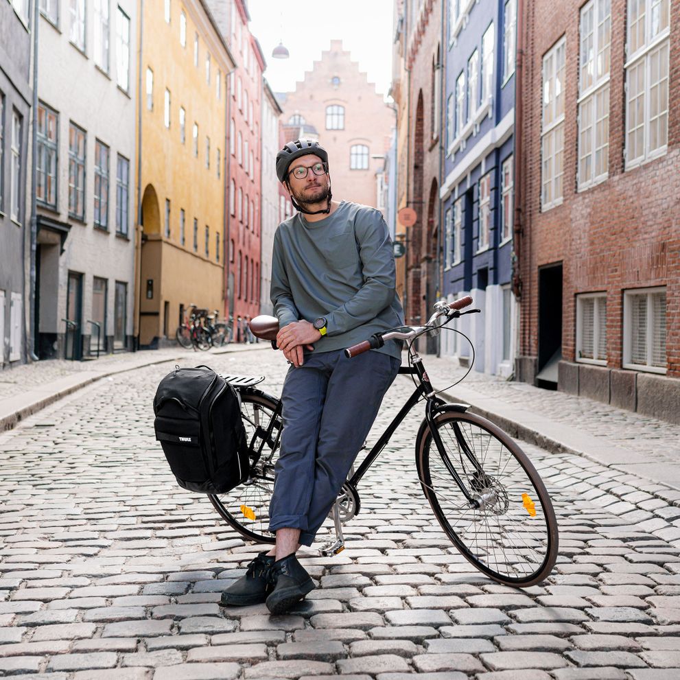 A man stands with his bike and the Thule Paramount bike bag on a colorful street.