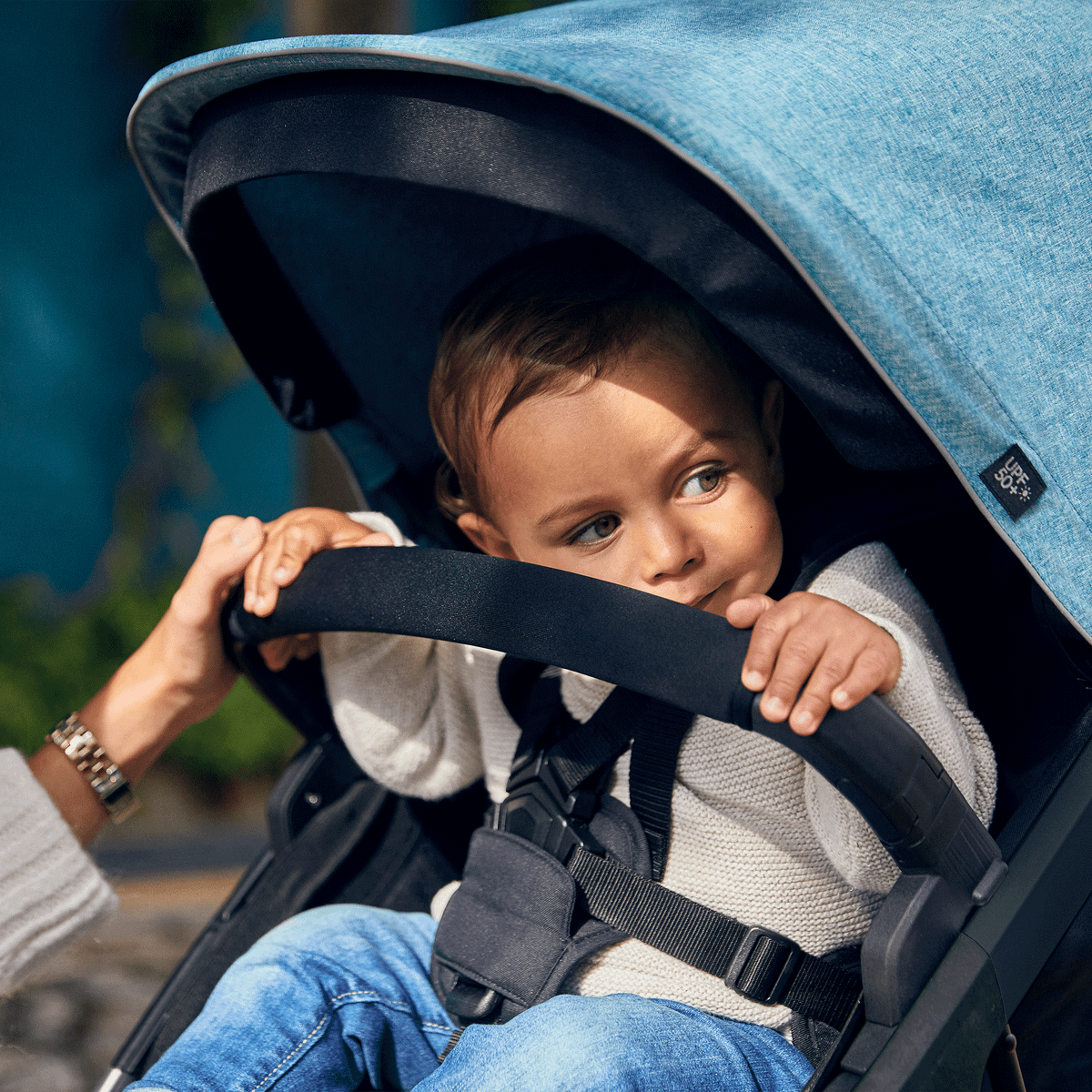 A child sits in a blue stroller holding on to the Thule Spring Bumper Bar.