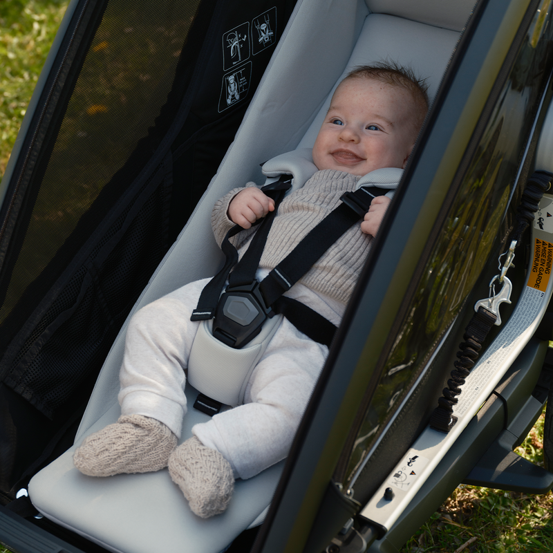 A baby secured in a Thule Chariot infant sling inside a Thule Chariot bike trailer.