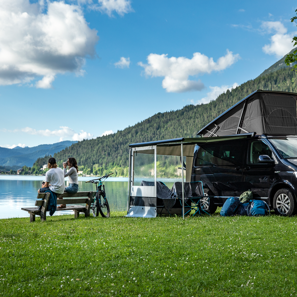 A black van parked next to the lake with a Thule Rain Blocker Side awning side wall.