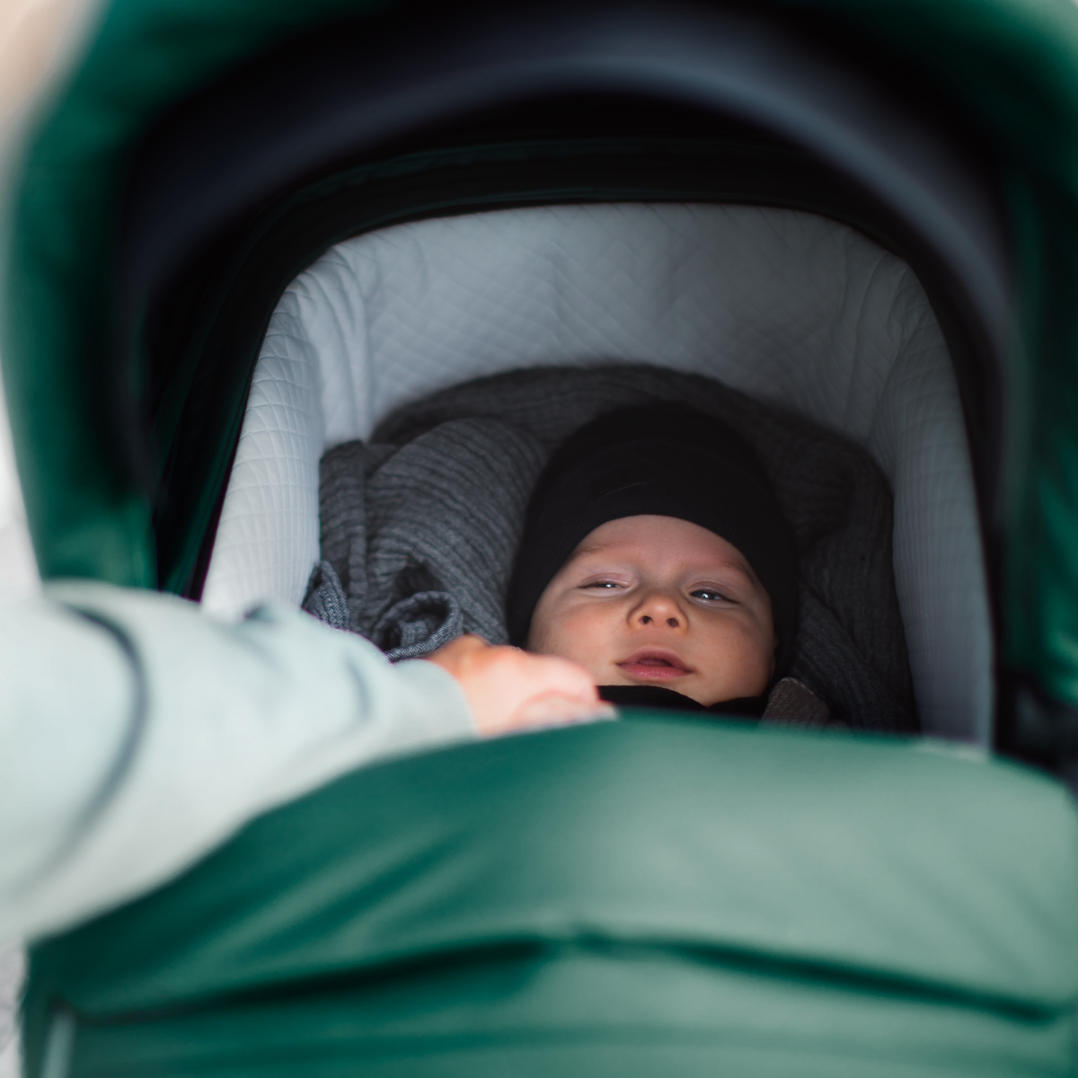 A close-up of a baby nestled inside a green Thule Sleek Bassinet.