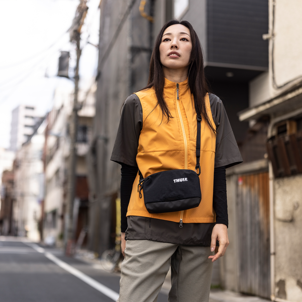 Woman walks down a street with a Thule Paramount 2L crossbody bag.