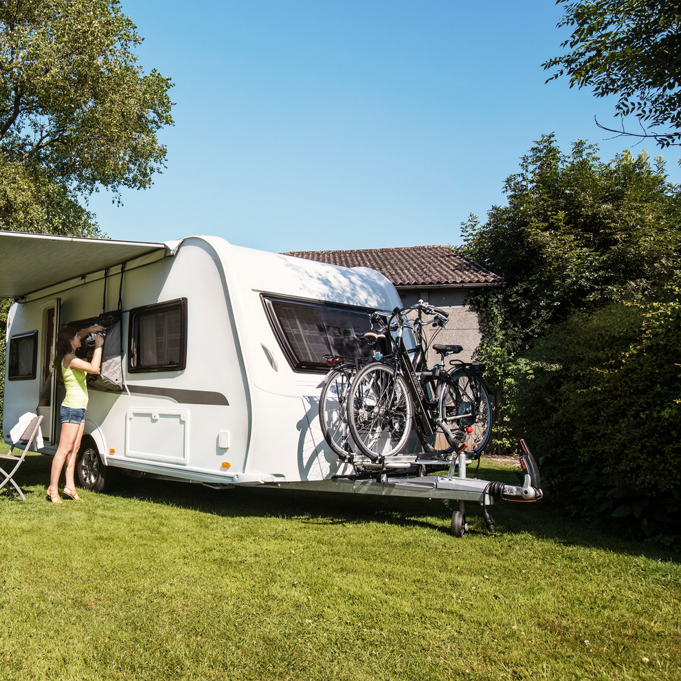 A caravan is parked in the grass with bikes installed on the caravan bike rack.