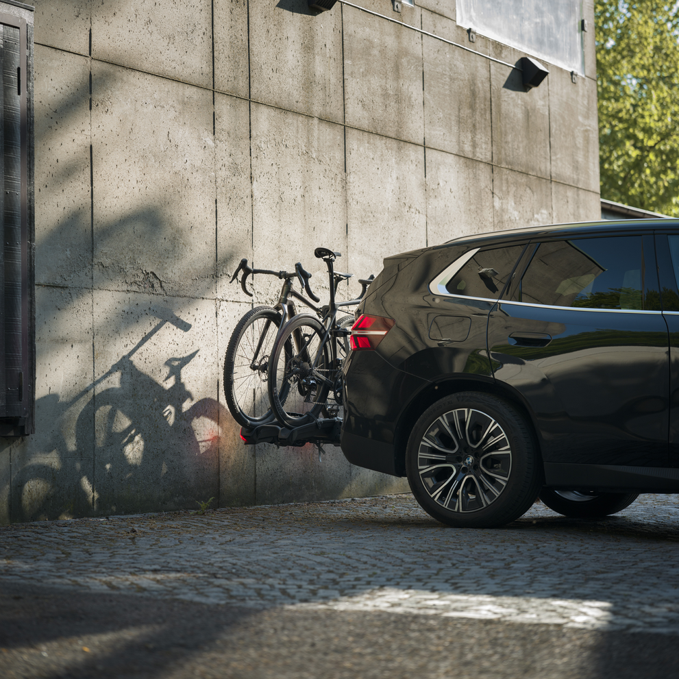 A SUV parked on cobblestones with a Thule Epos ParkSecure carrying two bikes against a concrete wall backdrop.