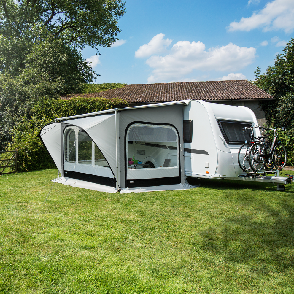 A motorhome parked in the grass on a sunny day with a Thule QuickFit rv awning tent.