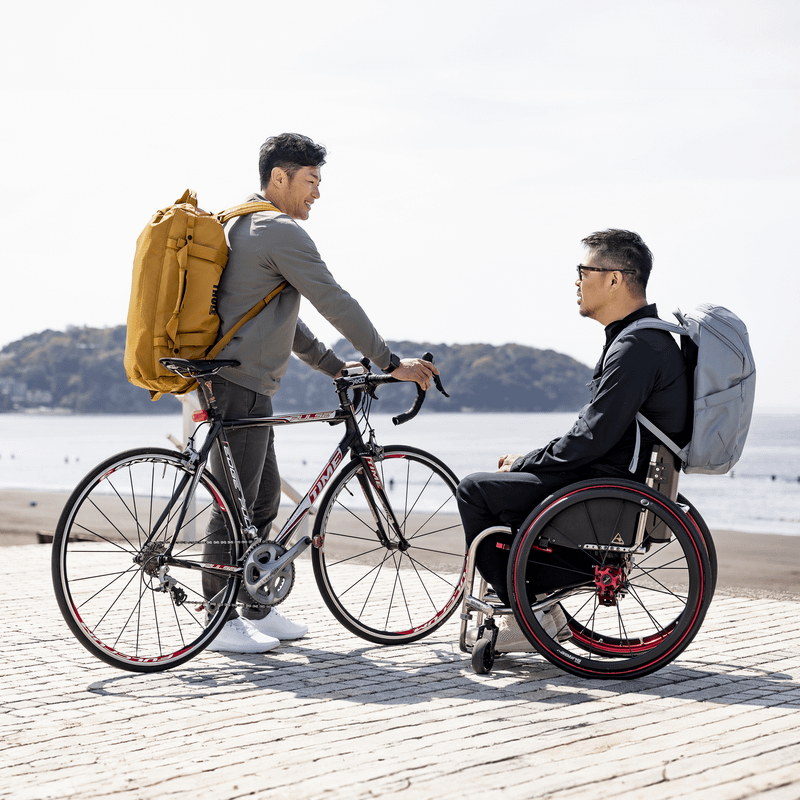 Two men stand next to the water carrying a Thule Chasm backpack and duffel.