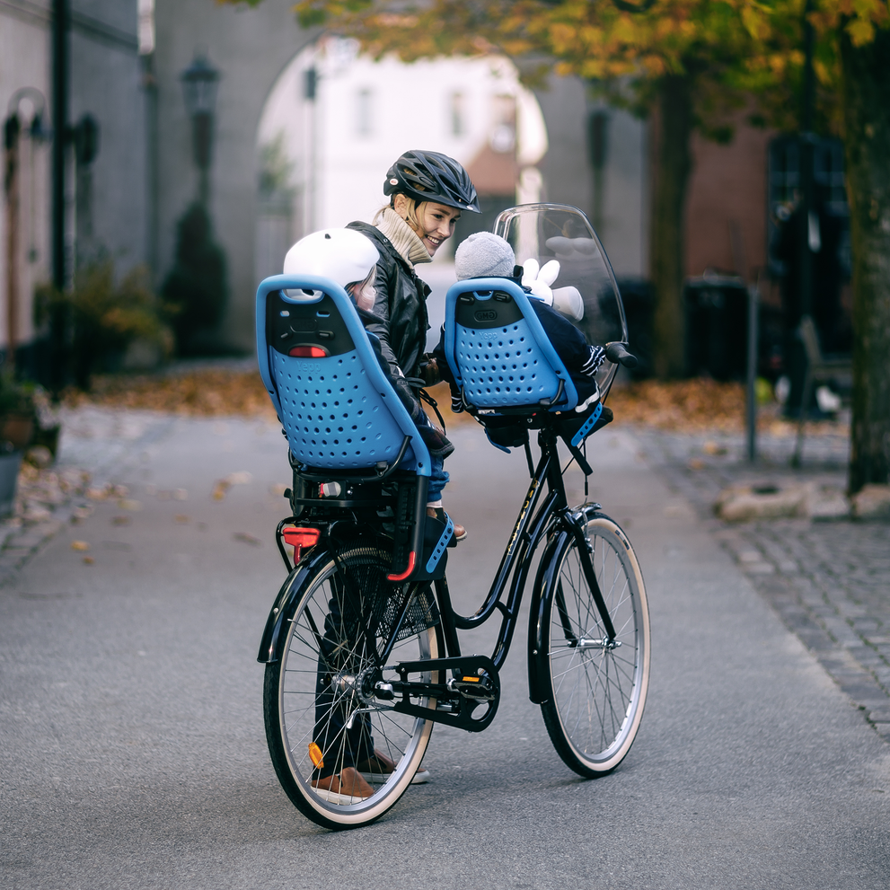 A woman strolls with her kids in child bike seats, a rear and front Thule Yepp Mini child bike seat.