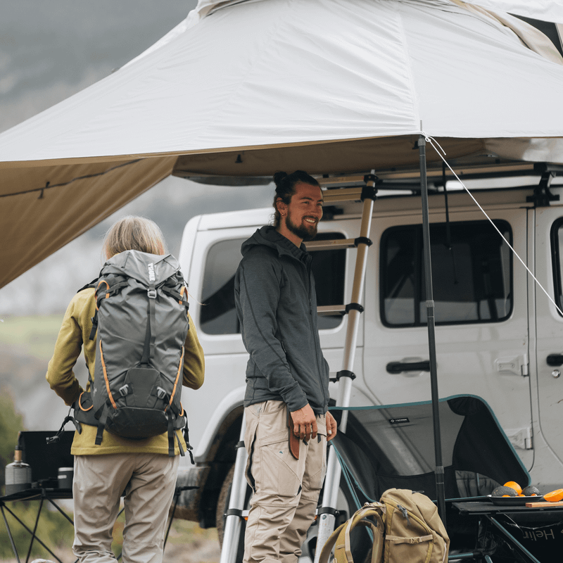 A man and a woman is standing under the awning of a roof top tent