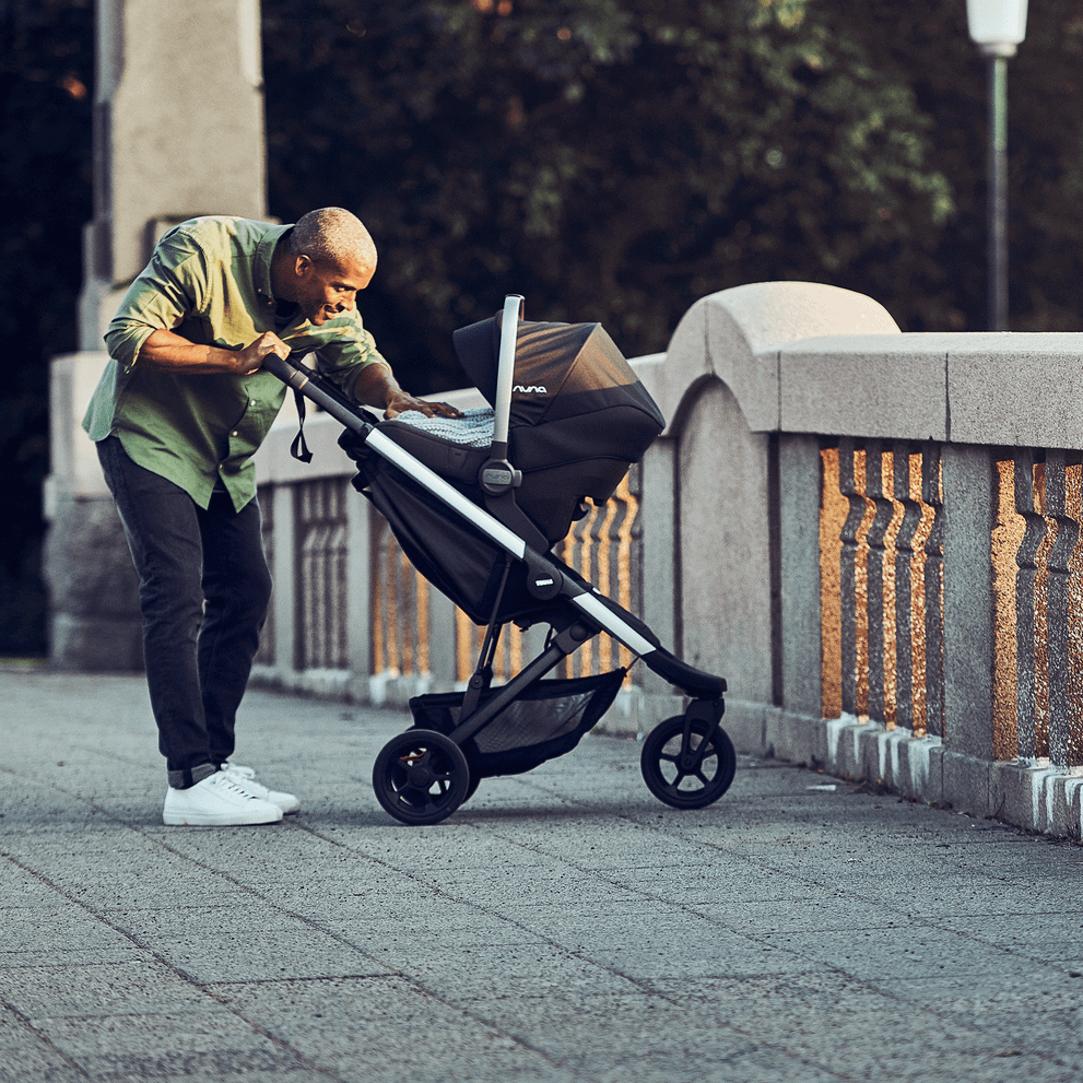 A man on a concrete bridge tends to his baby in a Thule Spring stroller with car seat attached.