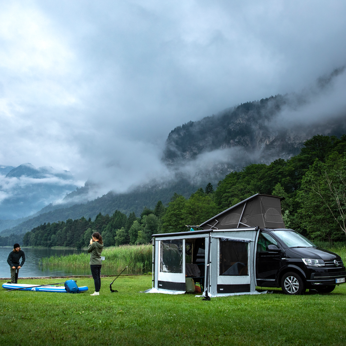 A van parked by a lake and a mountain with a Thule Residence G3 van awning tent.