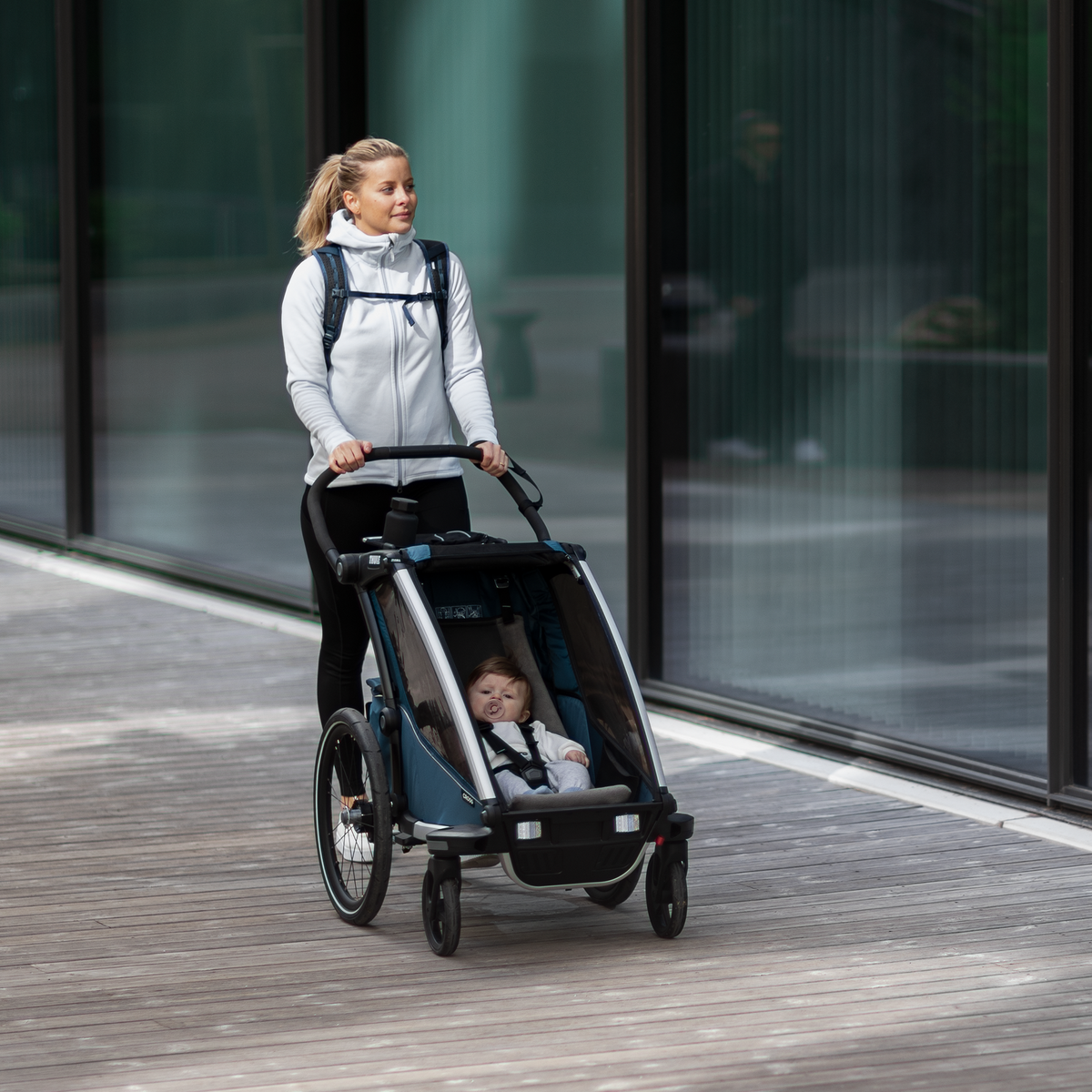 A woman strolls down the street with a baby in her child bike trailer using a Thule Chariot Infant Sling.
