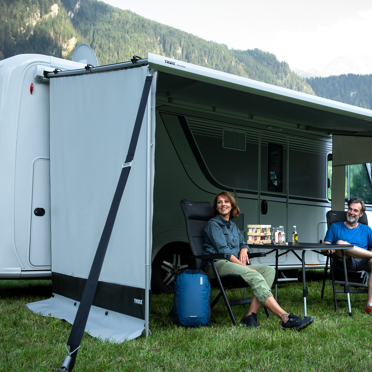 A couple sit next to their motorhome with a Thule View Blocker Side awning side wall.