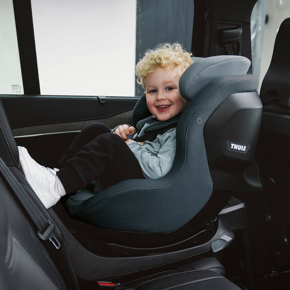 Ein lächelndes Kind, das in einem Thule Elm Kindersitz in einem Fahrzeug sitzt.