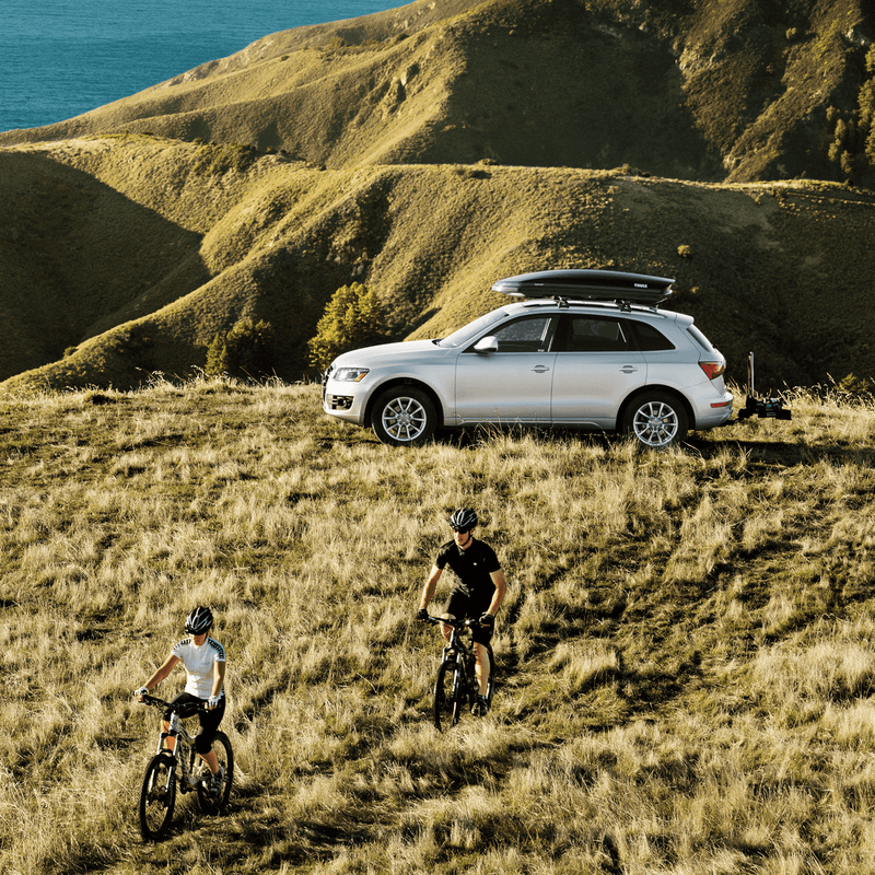 A car with a bike carrier is parked on a hill by the oceanfront.