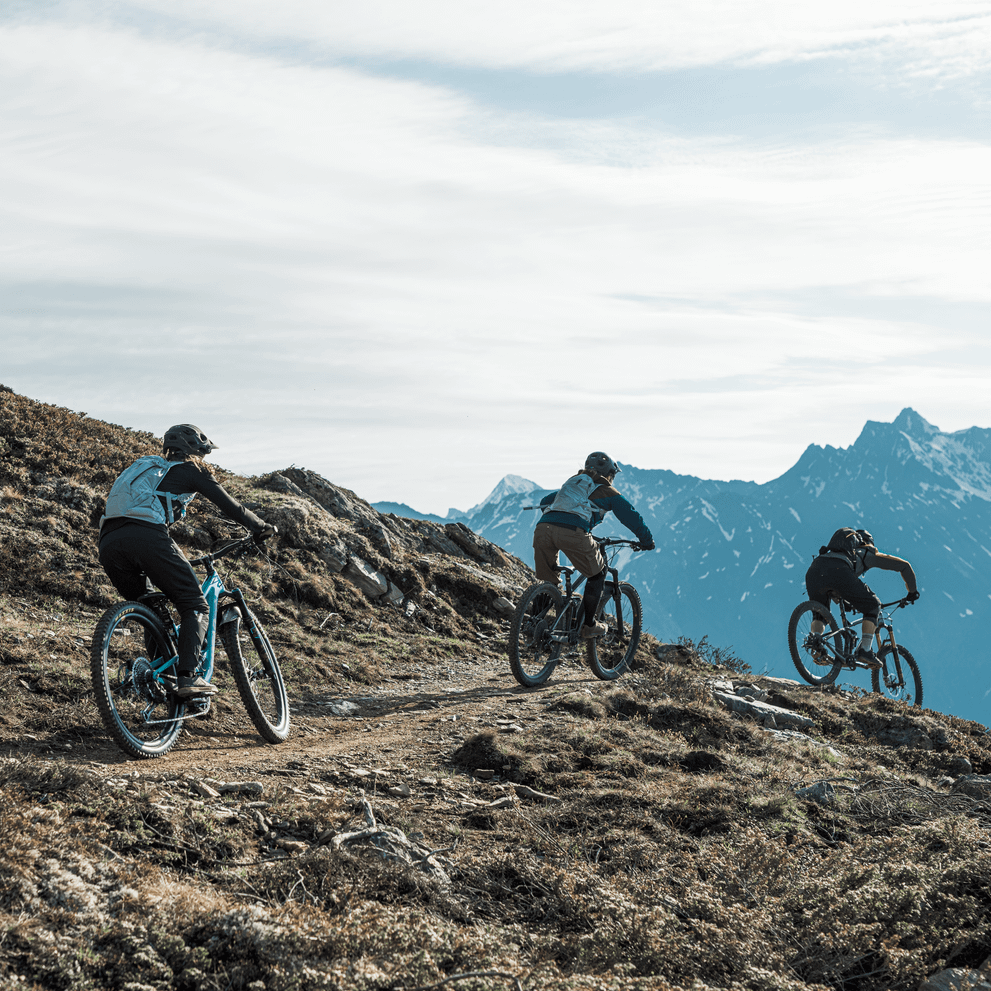 Three cyclists ride on a mountain path carrying blue Thule Vital 3L Women's Hydration Backpacks.