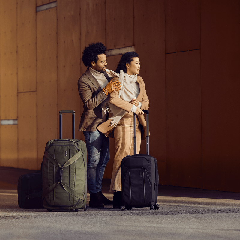 A man and a woman stand under a tunnel, with Thule Crossover 2 Wheeled Duffel suitcases.