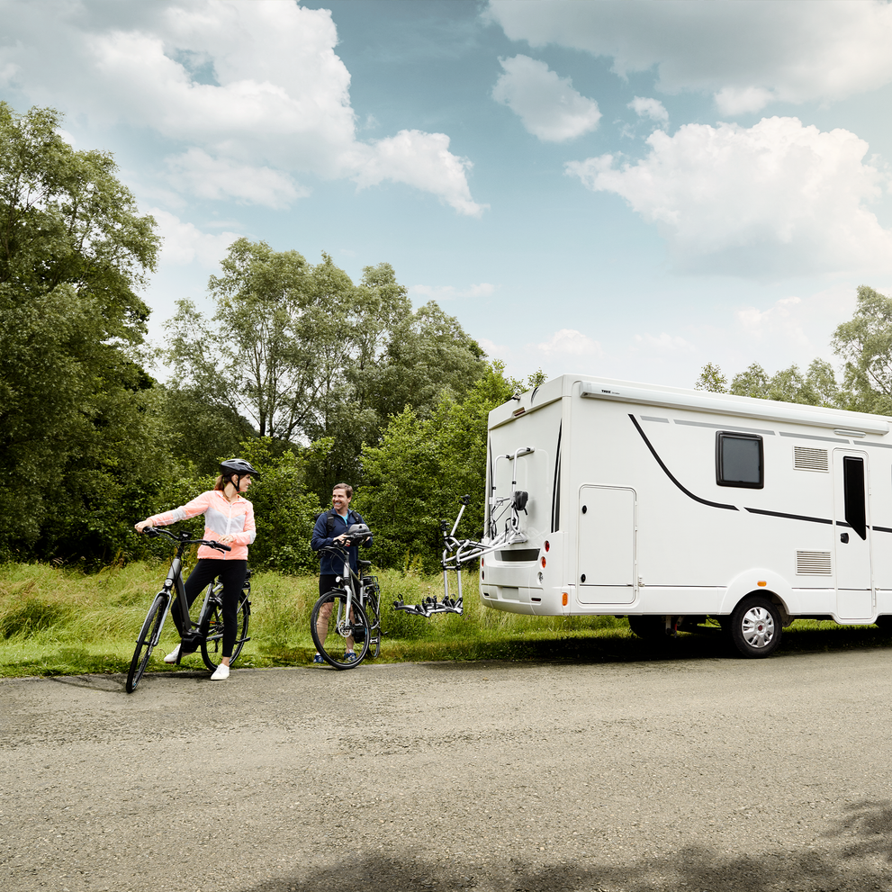 A motorhome parked in a park with cyclists behind it and a Thule Lift V16  rv bike rack.