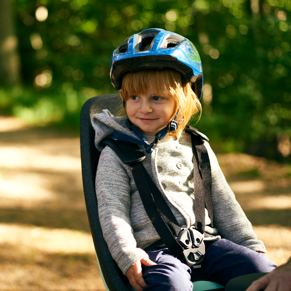 In a park, a little child sits in a Thule Yepp Nexxt child bike seat.