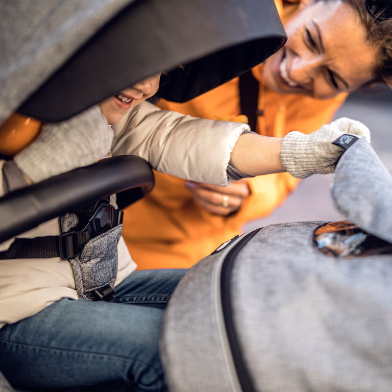 A woman peers inside the gray Thule Sleek Sibling Seat canopy to see her child.