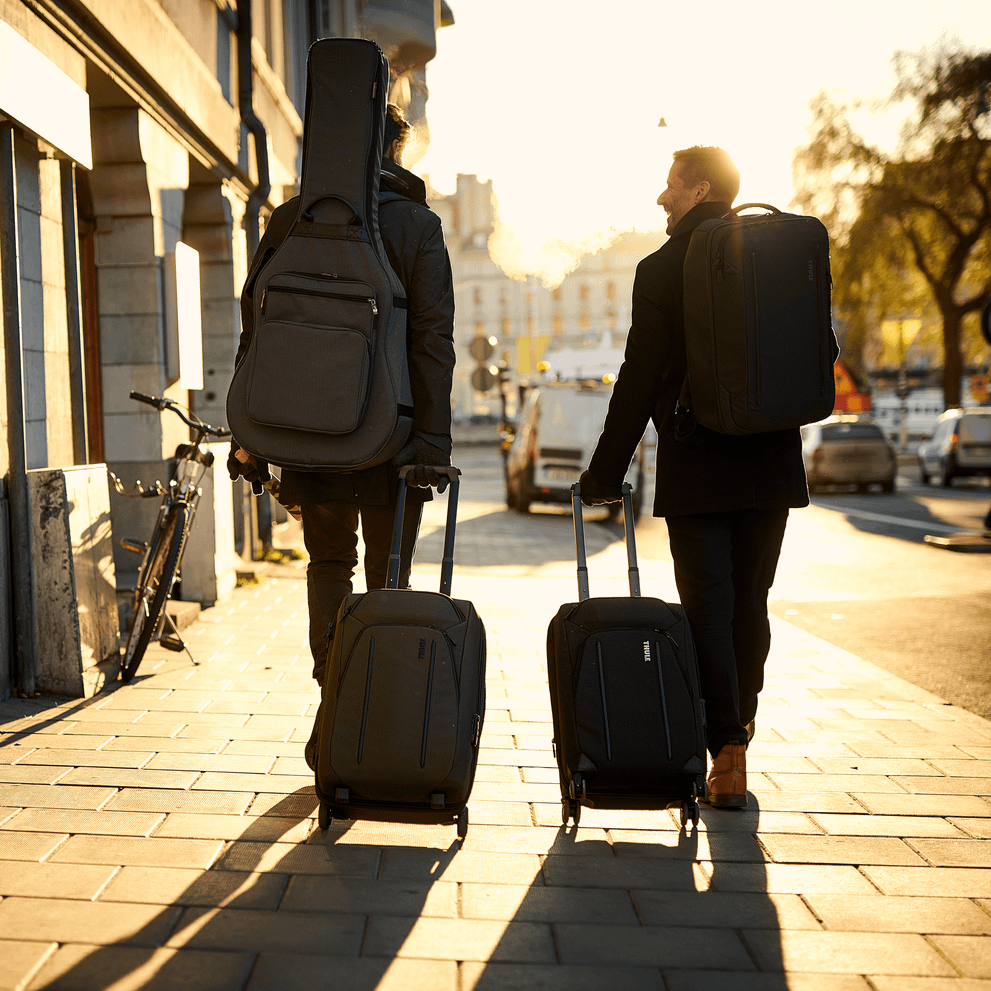 In the sunset, two people walk down a street with Thule Crossover 2 Carry-On suitcases.