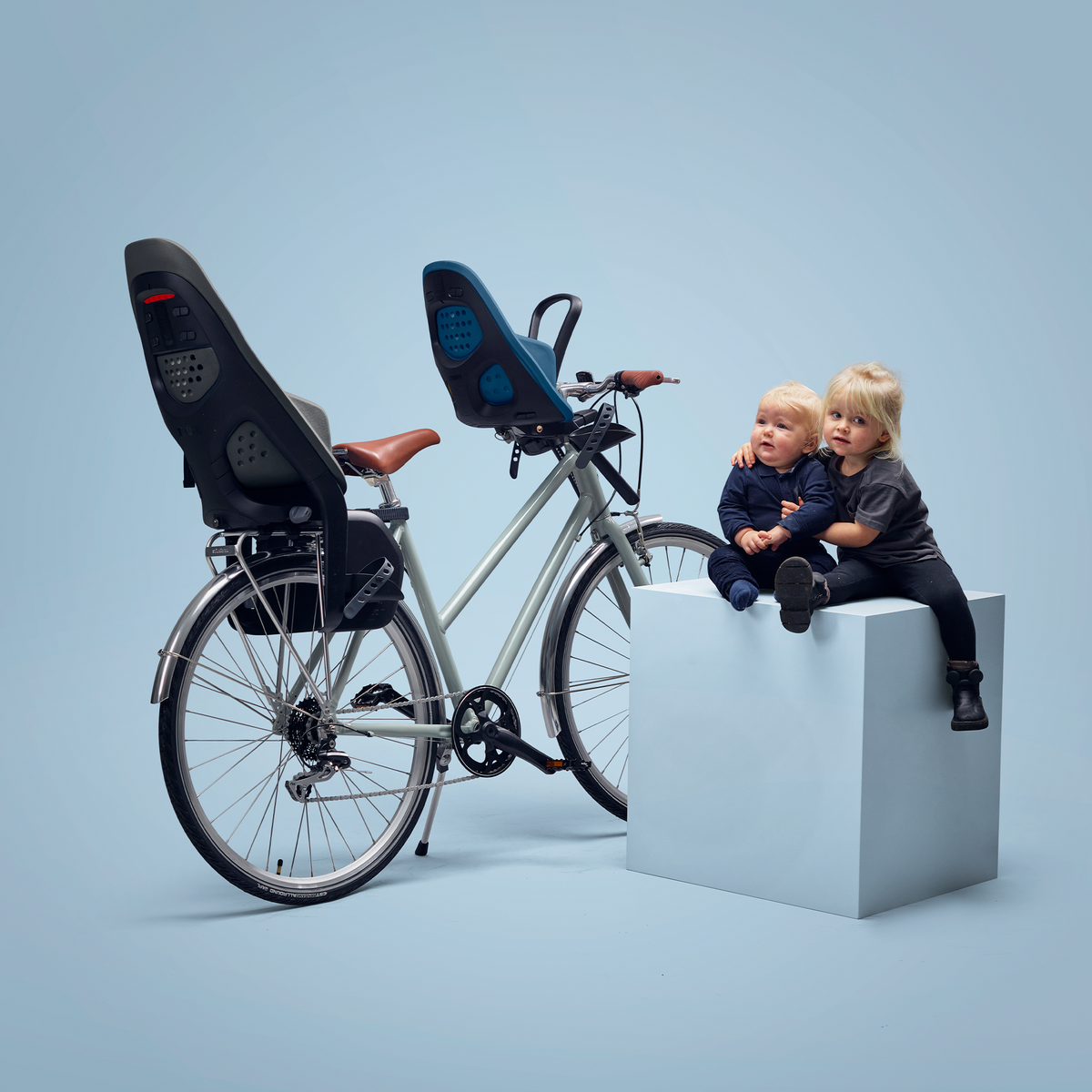 A blue bike, blue background and kids in a blue Thule Yepp 2 Maxi and Mini baby bike seat.