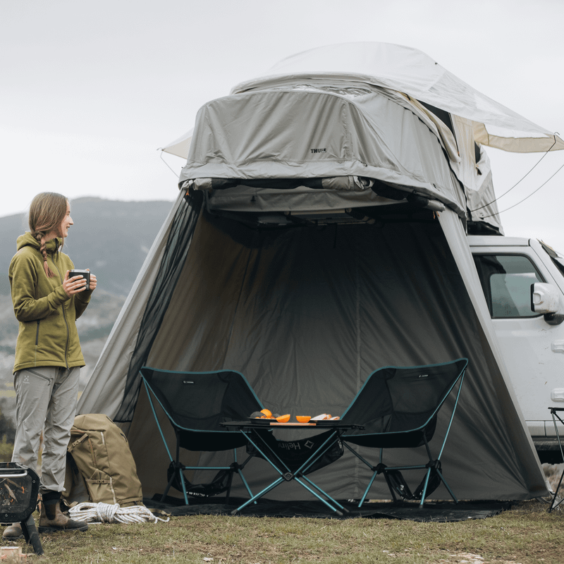 A man and a woman stands in front of a car with a roof top tent that has an annex