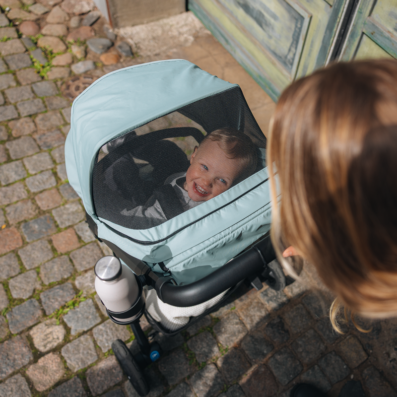 Child sleeping in Thule Spring 2 bassinet with mesh cover while woman looks on.