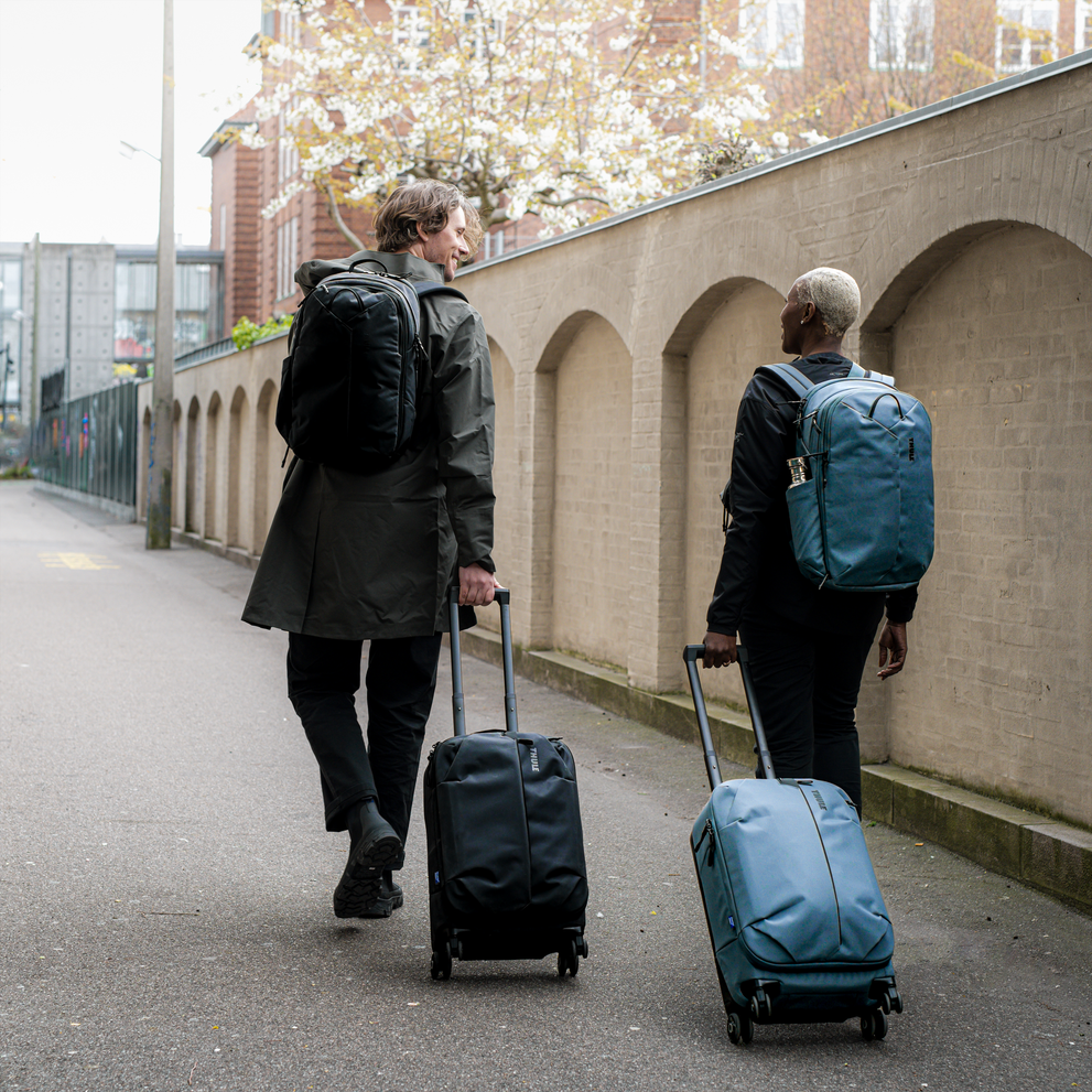 Two people walk down a street pulling Thule Aion carry-on suitcases and carrying Thule Aion backpacks.
