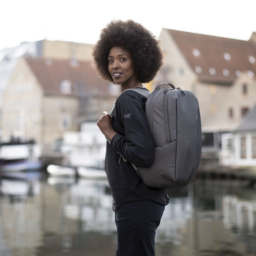 A woman stands by a canal in the city with a Thule Subterra backpack in Vetiver Gray.