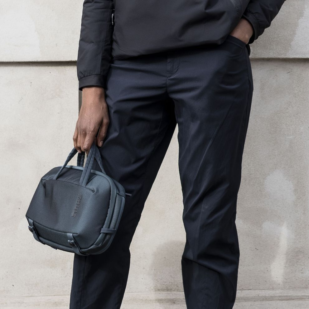 A close-up of someone wearing all black, holding a blue Thule Subterra Crossbody 5L.