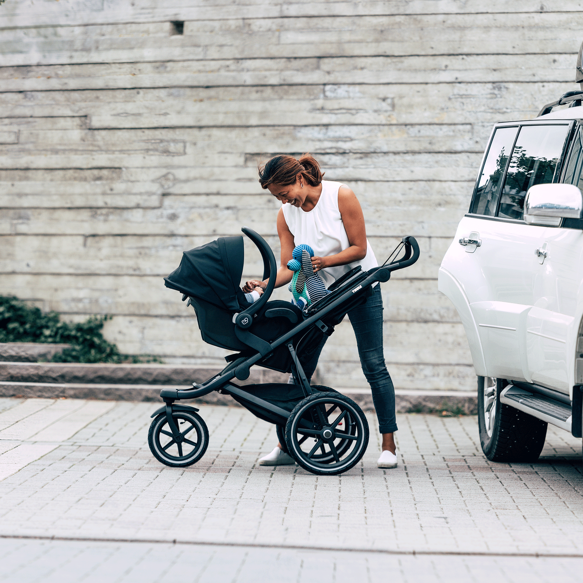 A woman tends to her baby in a car seat attached to the Thule Urban Glide 2 all-terrain stroller.