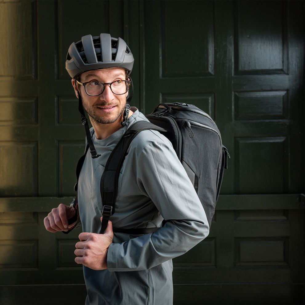 A man with a black helmet carries a black Thule Paramount bike backpack.
