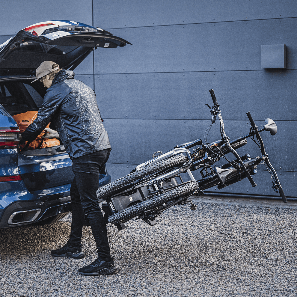 A man opens the trunk on  a car with the bike carrier Thule EasyFold XT 2