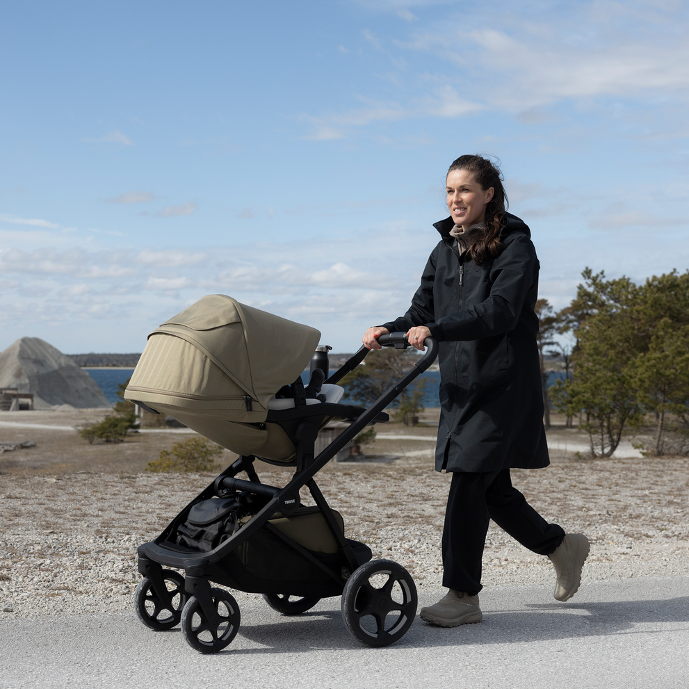 Adult pushing a Thule Charm stroller outdoors by the water.