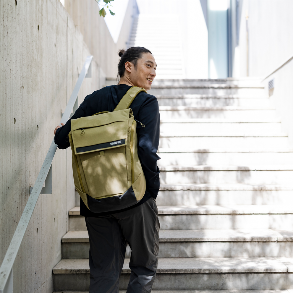 A man walks up sunny stairs with a Thule Paramount 27L.