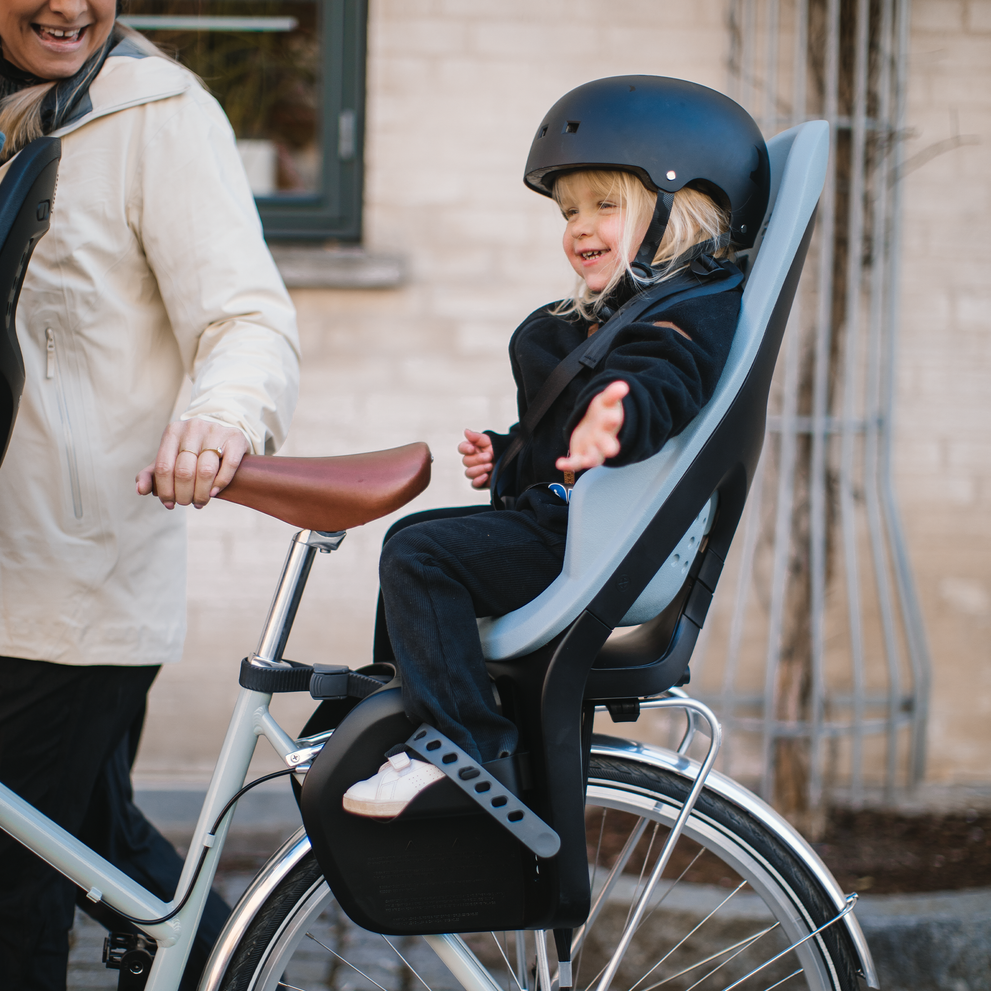 A smiling child sits in a blue Yepp 2 Maxi child bike seat.