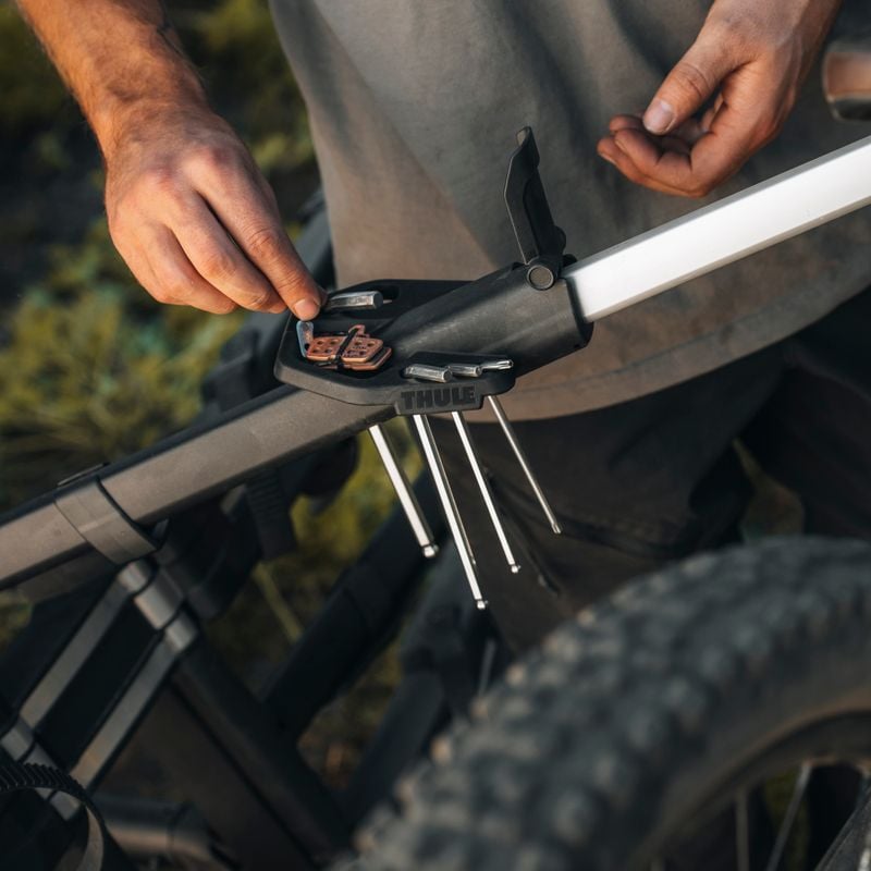 Close-up of arms and hands of a person handling bike repair tools on the Thule Epos bike repair holder.