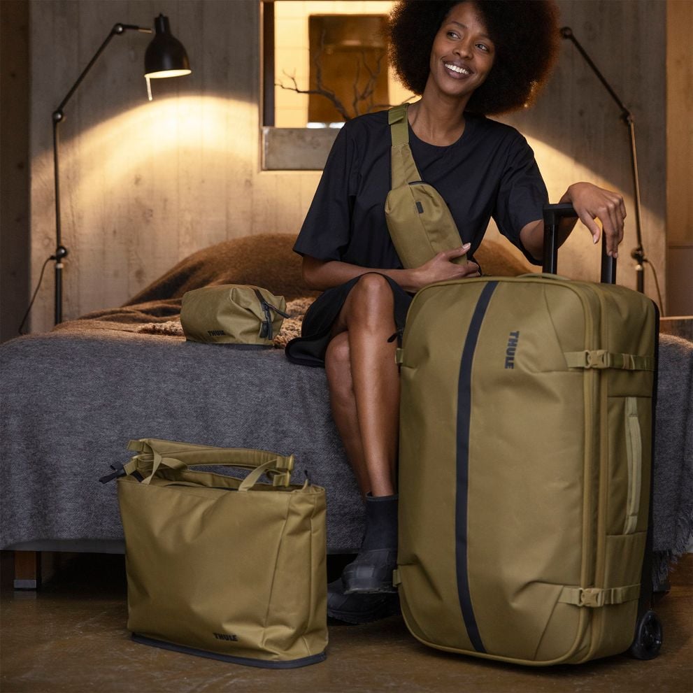 Person sitting on a bed with a Thule Aion carry-on suitcase and bags.